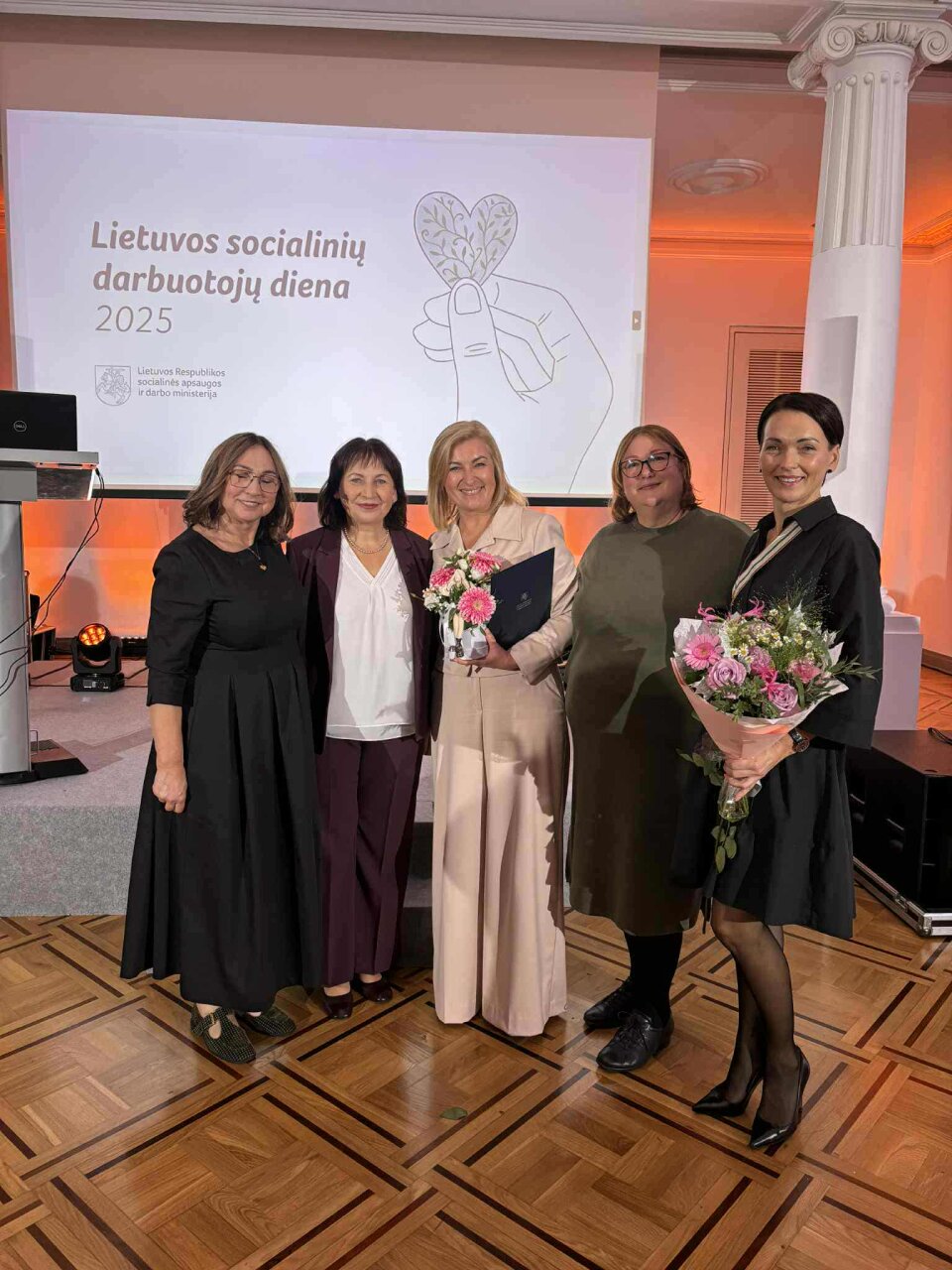 Šventės akimirka. Iš kairės į dešinę: Juratė Tamašauskienė (Lietuvos socialinių darbuotojų asociacijos prezidentė, Socialinių darbuotojų ir kitų socialinių paslauguų srities darbuotojų profesinių kompetencijų tobulinimo centro (PKTC) vadovė), Jūratė Zailskienė (Lietuvos Respublikos socialinės apsaugos ir darbo ministrė), Loreta Petrauskienė (Pasvalio rajono paramos šeimai centro direktorė), Virmanta Kvedarienė (Lietuvos socialinių darbuotojų asociacijos Panevėžio skyriaus pirmininkė) ir Jolanta Grybauskienė (Pasvalio socialinių paslaugų centro darbui su šeimomis padalinio vadovė)